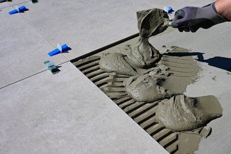 Close-up of a gloved hand applying mortar for ceramic tile installation outdoors.